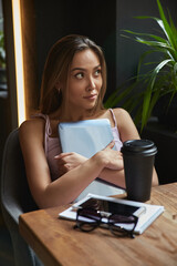 young asian stylish pretty woman sitting at table of coffee shop, holding laptop, having rest. beautiful lady sits at cafe with tablet. modern online education, distant work, remote job, lifestyle