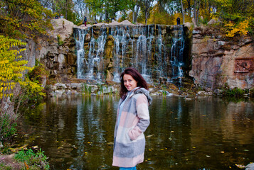 happy girl smiling in autumn coat on waterfall nature background