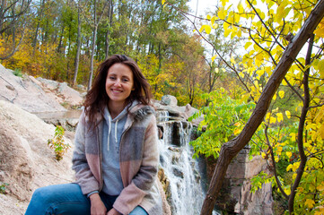 autumn nature. copy space. cheerful woman in coat sitting near waterfall.