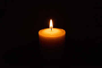 One single light candle burning brightly in the black background.Spiritual candle yellow flame....