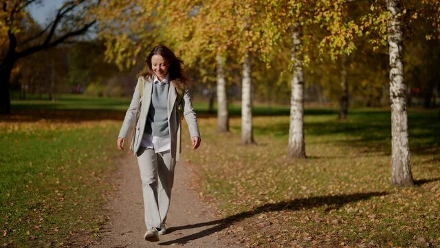 Happy beautiful adult woman walking outdoors. Carefree girl enjoys an autumn day in the park
