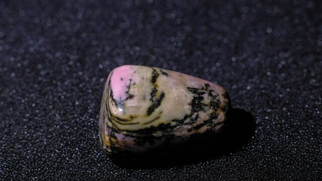 Natural gemstone polished rhodonite rotation 360 over black background. 4k. Macro shot.