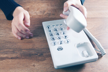 a woman dials a number on a home wired phone