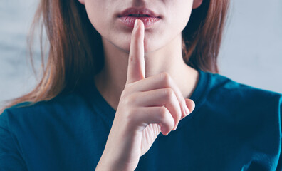 woman showing a sign of silence with her finger - obrazy, fototapety, plakaty