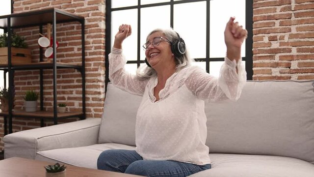 Middle age grey-haired woman smiling confident listening to music at home