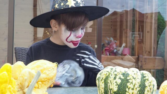 boy and scull, teenager wearing scary jocker or clown makeup and halloween costume with hat play with scull outdoor, selective focus. traditional american holiday party