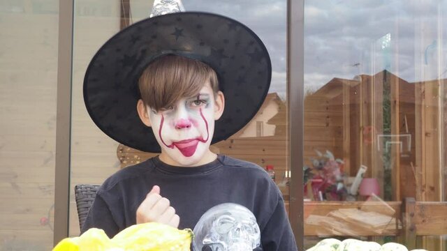 boy with Halloween costume, scary jocker or clown makeup holding wand outdoor. Horror concept of party