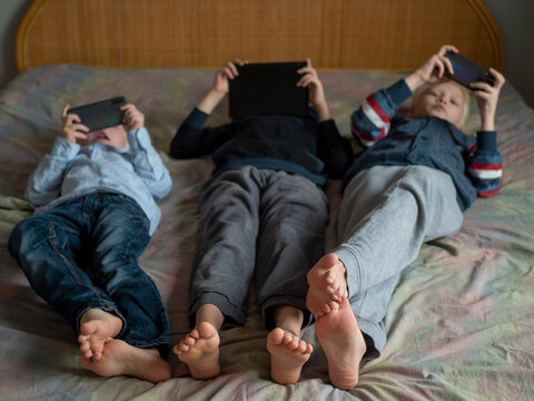 Three boys lie on couch and are passionate about devices