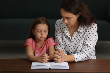 Mature woman with her little granddaughter praying together over Bible at home