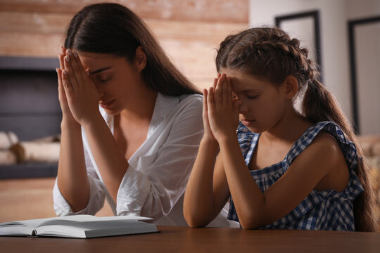 Young woman with her little daughter praying together over Bible at home