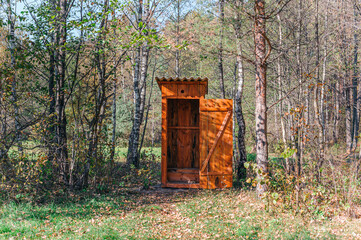 Opened wooden WC toilet cabin in a golden forest national park, close-up. Autumn landscape....