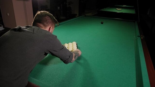 Close-up of a brutal man playing Russian billiards in a bar, he puts a triangle with balls before the game.