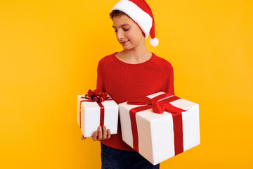 Pensive boy in a Christmas hat and a gift in his hands. Thoughtfully thinks what is inside gifts. On a yellow background