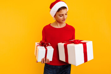 Pensive boy in a Christmas hat and a gift in his hands. Thoughtfully thinks what is inside gifts. On a yellow background