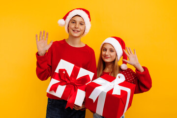 Christmas two friends, a boy and a girl in santa claus hats and gifts, on a yellow background. christmas eve