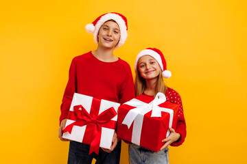 Christmas two friends, a boy and a girl in santa claus hats and gifts, on a yellow background. christmas eve new year