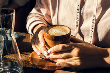 Fototapeta na wymiar cappuccino cup in women's hands in a cafe