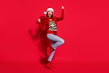 Photo of lucky funny young woman wear print sweater rising fists celebrating new year isolated red color background