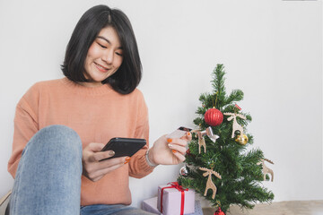 young woman sit on floor, using mobile phone, and holding credit card for christmas online shopping