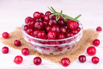 Fresh cranberries in a transparent glass bowl on a white background.
Close-up.