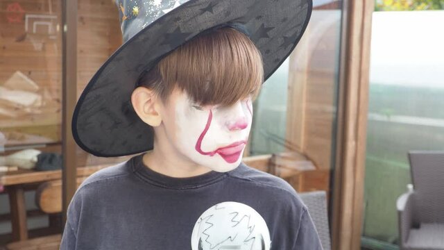 boy with Halloween costume, scary jocker or clown makeup holding wand outdoor. Horror concept of party
