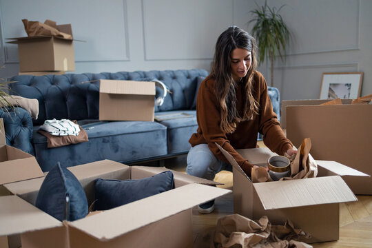 Young woman wrapping a vase while packing boxes before moving out of the apartment.