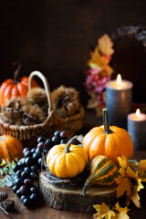 Thanksgiving celebration concept with traditional seasonal decorations like pumpkins, fall leaves, grapes, chestnuts and lit candles against dark rustic background