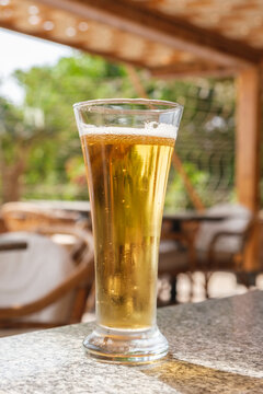 Vertical image of a glass with light beer on the table in a summer cafe. Soft alcoholic beverages on a hot day. Bar at the resort.