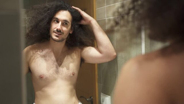 Young adult smiling and checking afro hair in the mirror shirtless