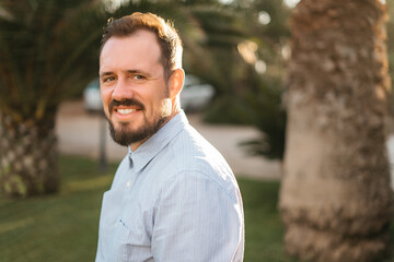 Portrait of happy mature man looking at camera outdoor. Senior businessman with beard feeling confident at sunset. Closeup face of business man smiling with city in background.