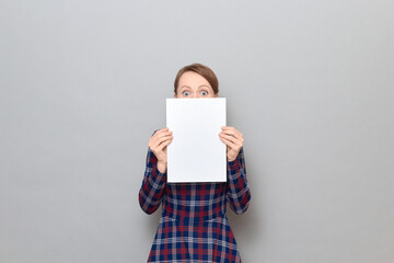 Excited woman is peeking out from behind paper sheet with widened eyes