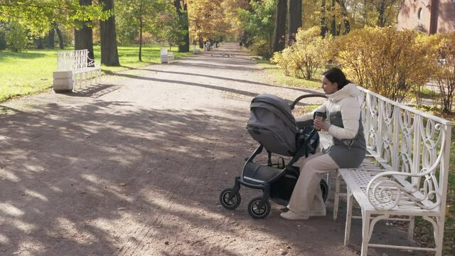 Mother with baby stroller on a walk in the park in autumn, mom sitting on park bench in Catherine Park in the town of Tsarskoye Selo, Pushkin. High quality 4k footage