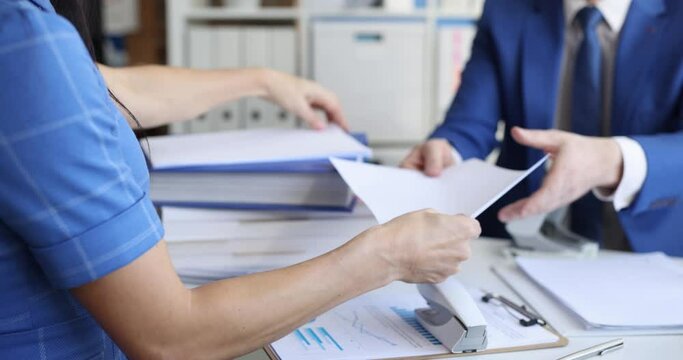 business man and woman are sitting at the table and sorting documents with a stapler
