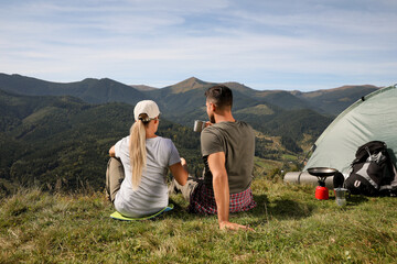 Fototapeta na wymiar Couple enjoying mountain landscape near camping tent, back view