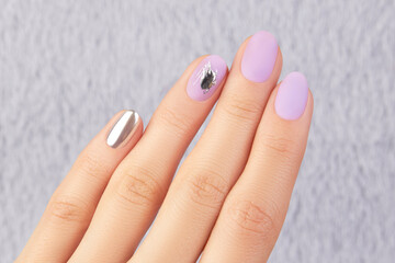 Naklejka premium Close up womans hand with matte lavender nail design on gray furry background