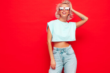 Young beautiful smiling female in trendy summer clothes. Sexy carefree woman posing near red wall...