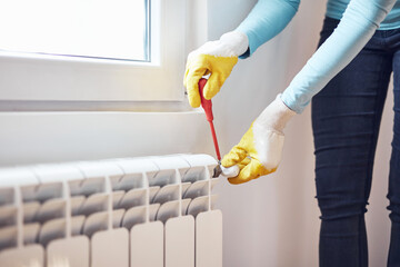 Handyman with gloves fixing and bleeding air from central heating gas radiator system at home.