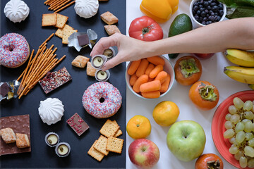 Healthy and unhealthy food concept, fruits and vegetables vs donuts, sweets and chocolate with woman's hand. Top view