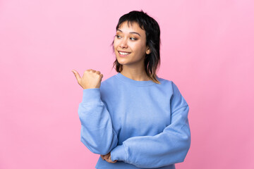 Young Uruguayan woman over isolated pink background pointing to the side to present a product