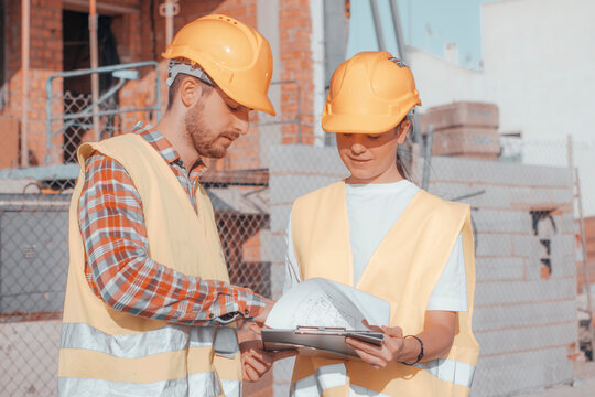Equipo joven de arquitectos de una constructora para una inmobiliaria trabajando en equipo con cascos mientras revisan los planos de la construcci&oacute;n de obra