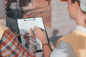 Equipo de arquitectos con cascos de una constructora realizando un análisis de maquetas y planos...