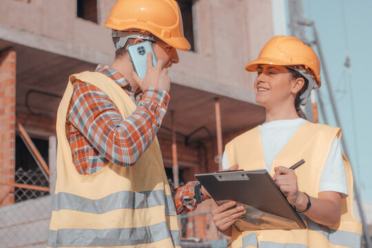 Empleados de construcci&oacute;n de ingenier&iacute;a y arquitectura realizando una llamada de su tel&eacute;fono m&oacute;vil para contactar con la inmobiliaria y consultar los planos e ideas 