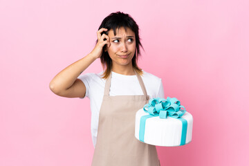 Uruguayan Pastry chef holding a big cake over isolated pink background having doubts and with confuse face expression