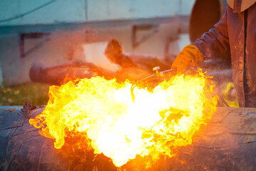 Welder's hands in protective gloves during operation. Cutting a metal pipe on the street during the day with acetylene welding. Close-up. Industrial background. Construction site.