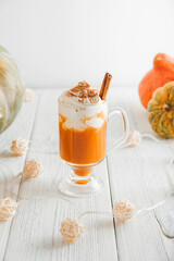 Cup with foam and cinnamon on background of pumpkins. Pumpkin autumn warming drink close-up and copy space...