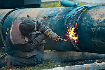 The welder cuts large metal pipes with ocetylene welding. A worker on the street cuts large-diameter pipes during the day and sparks and fire fly.