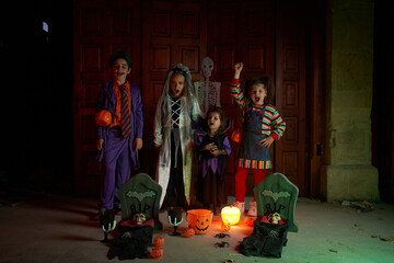 Obraz na płótnie Canvas Kids in Halloween costumes near glowing pumpkins and decorative gravestones in darkness