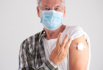 Portrait studio shot of old caucasian senior man patient wearing face mask showing with fingers number three as third doses of covid-19 coronavirus vaccine, looking at camera - obrazy, fototapety, plakaty