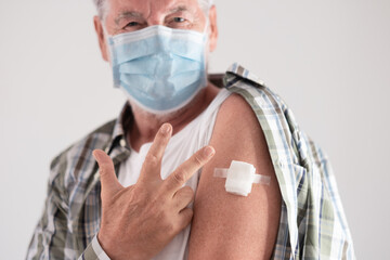 Portrait studio shot of old caucasian senior man patient wearing face mask showing with fingers number three as third doses of covid-19 coronavirus vaccine, looking at camera