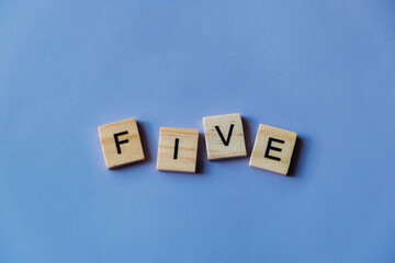 Number five laid out from tiles in words. Wooden tiles on a blue background with letters. View from above. Copy space.